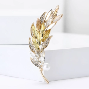 Elegant gold feather brooch with crystals and pearl on white geometric platform