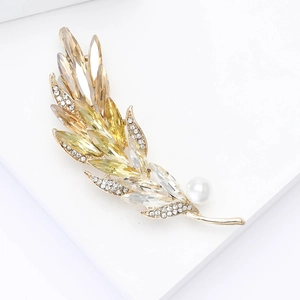 Detail of elegant gold feather brooch with champagne crystals and a white pearl accent