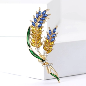 Macro view of golden wheat ear brooch with blue and yellow crystals and green enamel