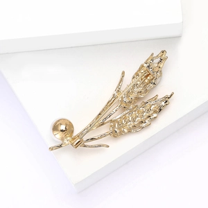 Détail d'une broche épi de blé dorée avec perle blanche sur un support blanc moderne