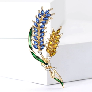 Detail of golden wheat brooch with blue and amber crystals on white display block