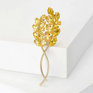 Détail d'une broche épi de blé dorée avec cristaux jaunes sur un support blanc