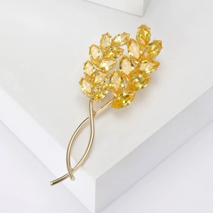 Détail d'une broche épi de blé dorée sertie de pierres jaunes sur fond blanc épuré