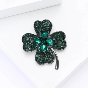 Détail d'une broche trèfle avec cristaux verts sur un support géométrique blanc