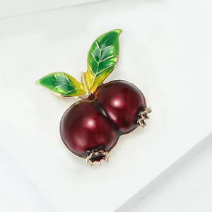 Elegant red enamel pomegranate brooch with gold trim and green leaves on white stand