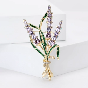 Broche lavande élégante dorée avec cristaux violets et pierres vertes sur un cube blanc