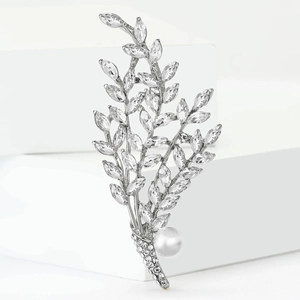 Elegant silver willow branch brooch with sparkling rhinestones and a white pearl on white pedestal