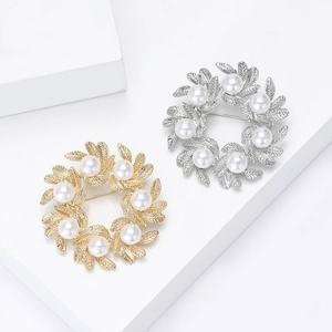 Elegant gold and silver leaf wreath brooch with pearls on white geometric stands