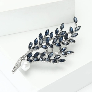 Detailed view of rhinestone willow branch brooch with blue crystal leaves and a white pearl