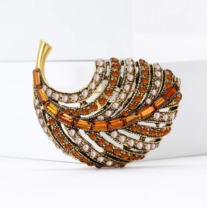 Elegant gold-tone leaf brooch with amber rhinestones on a white geometric stage
