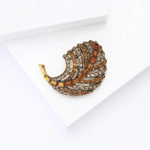Macro detail of golden alloy leaf brooch with sparkling amber and champagne rhinestones