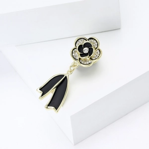 Macro shot of camellia brooch featuring black white enamel with ribbon pendant and rhinestones