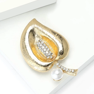 Detailed view of leaf-shaped gold brooch with radiant texture, rhinestones and large pearl