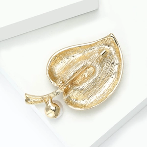 Detail of the golden leaf brooch back showing metallic texture, pearl and clasp