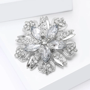 Elegant silver flower brooch with sparkling crystal rhinestones on a white geometric stand