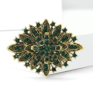 Macro view of vintage gold finish brooch with emerald green rhinestones and intricate details
