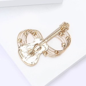 Close-up of golden guitar brooch with music notes and rhinestones on white pedestal