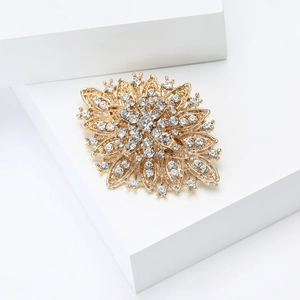 Macro shot of gold floral brooch with sparkling rhinestones on a white geometric stand