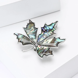 Elegant maple leaf brooch with iridescent shell inlay on minimalist geometric stand