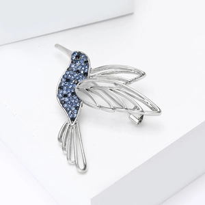 Macro detail of silver hummingbird brooch with gradient blue rhinestones on a white stand
