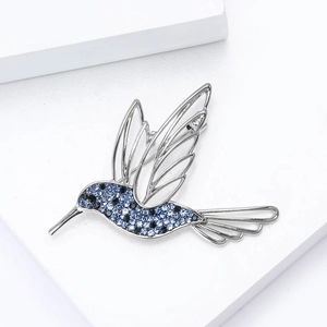 Detail of a hummingbird brooch with blue crystals on a white geometric base