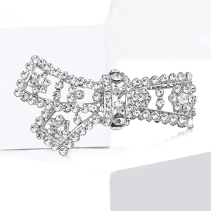 Elegant silver bow brooch with sparkling rhinestones on a minimalist white stone pedestal