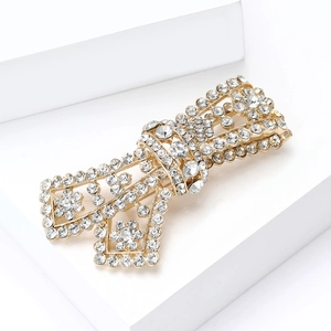 Close-up of golden bow brooch with sparkling rhinestones on a white geometric stand