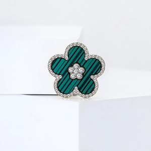 Elegant flower brooch with green striped petals and crystal border on white pedestal