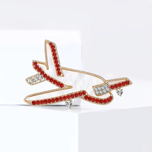 Elegant gold airplane brooch with pearl shell finish and sparkling red rhinestones