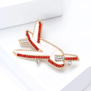 Elegant gold airplane brooch with red rhinestones and white shell inlay on a white cube