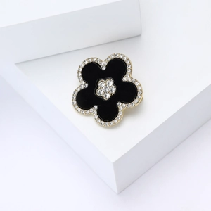 Detail of black enamel flower brooch with gold plating and sparkling zircon crystals