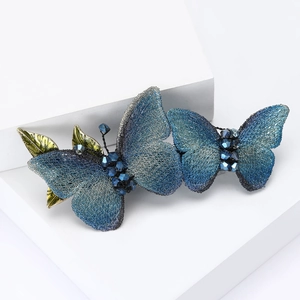 Elegant blue fabric butterfly hair clip with crystal beads and green leaves on white base
