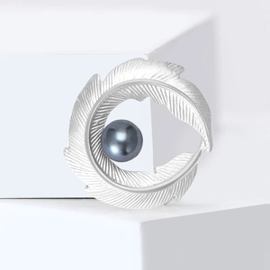 Matte silver curved leaf brooch with a dark grey pearl on a minimalist white block