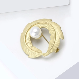 Detailed view of matte gold leaf brooch with a central white pearl on a white background