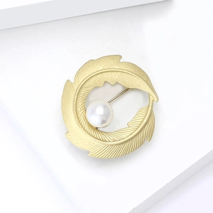 Detail of matte gold curved leaf brooch featuring a centered white pearl decoration