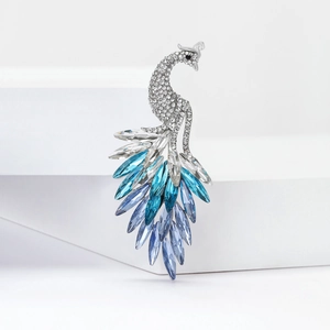 Elegant silver peacock brooch with blue gradient crystals and marquise gems on white pedestals