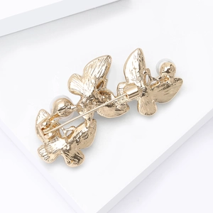Detail view of the golden butterfly brooch showing the secure pin back and pearl accents