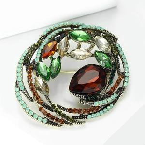 Detail of vintage bird nest brooch with deep red teardrop gem and multicolor crystals