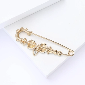Detail of a golden alloy safety pin brooch with a small rhinestone heart pendant