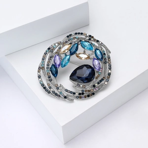 Macro detail of bird nest brooch with blue pear-shaped crystal and colorful rhinestones