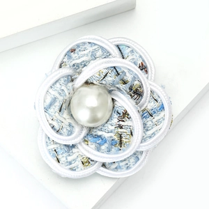 Macro shot of camellia brooch in light blue tweed fabric with a central pearl accent