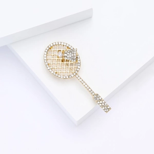 Macro detail of gold-plated tennis racket brooch with white crystals and a pearl ball