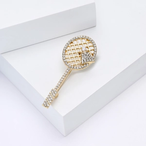 Macro shot of gold-plated tennis racket brooch with sparkling rhinestones and white pearl