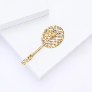 Close-up of golden tennis racket brooch with hollow grid design on white props