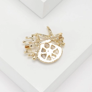 Macro view showing the gold-plated metal back and safety pin of the shell brooch