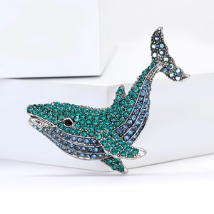 Silver whale brooch with blue and green rhinestones displayed on a white stand