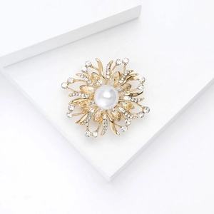Vue détaillée d'une broche fleur dorée avec perle blanche et strass brillants scintillants