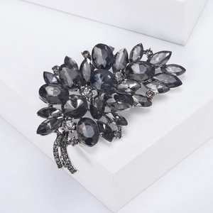 Macro d'une broche en alliage argenté avec strass gris foncé sur un socle blanc épuré
