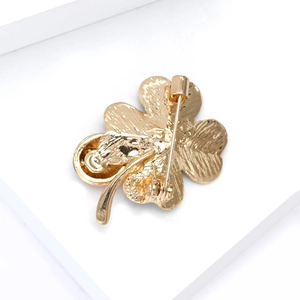 Detail view of the secure pin clasp on the back of a gold clover brooch with textured metal
