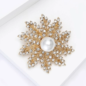 Détail macro d'une broche flocon dorée avec perle blanche et strass brillants scintillants